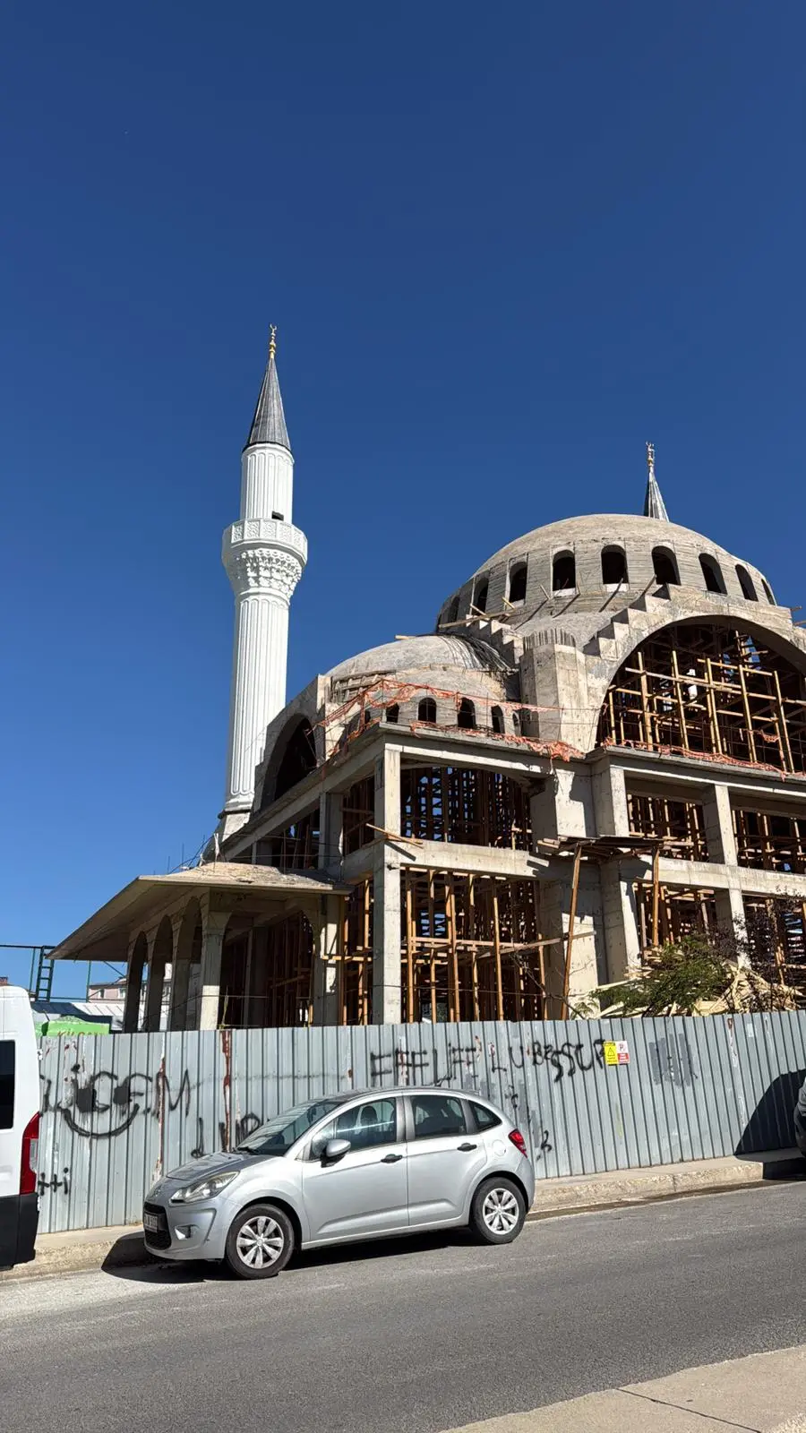 Sokak kotundan cami ve minare — kaba yapı ve ahşap kalıp iskelesi
