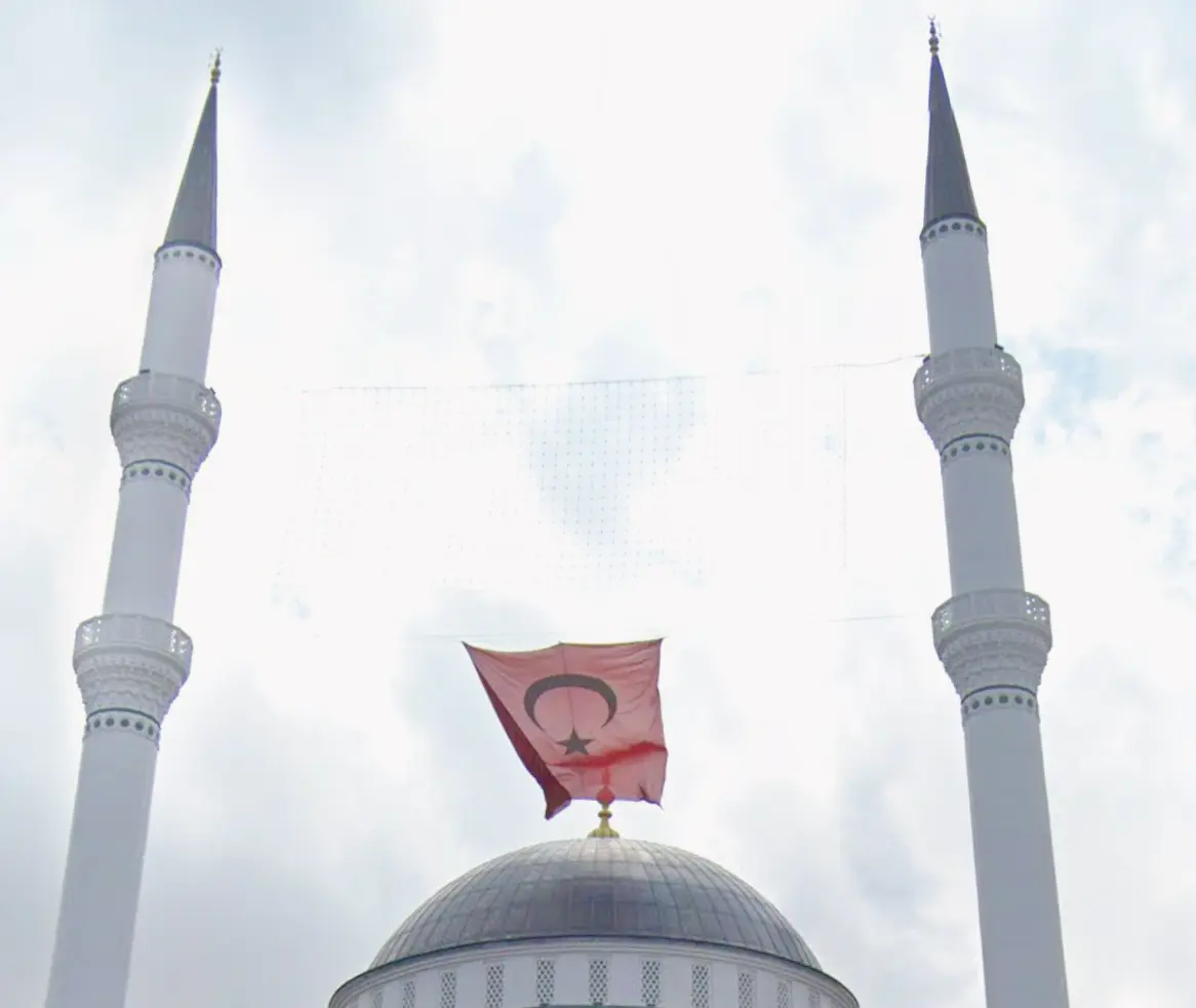 İki minarenin şerefe bilezikleri ve aralarına asılan bayrak, altta kubbe alemi