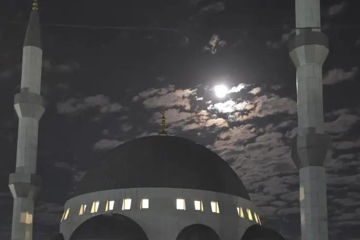 Gün batımında Melbourne Camii — aydınlatılmış cephe, iki minare ve hilal