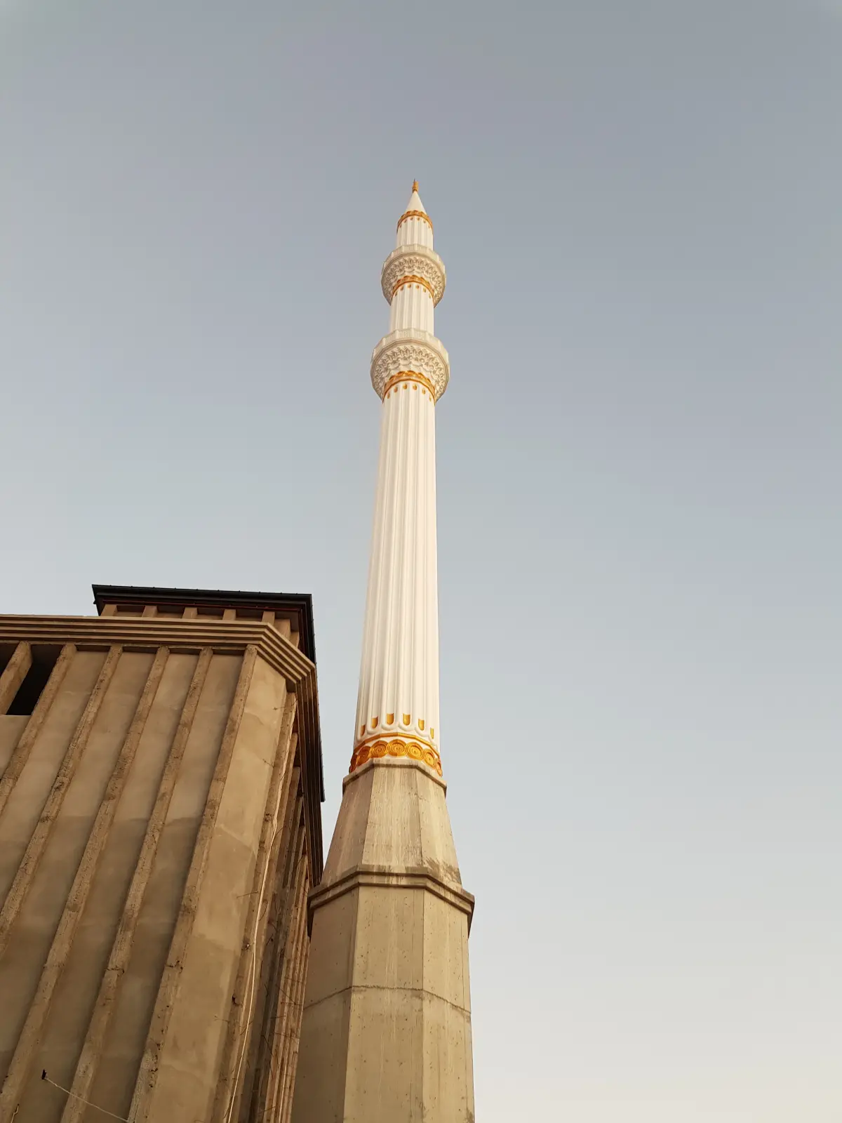 Tamamlanan çift şerefeli minare — yivli beyaz gövde ve altın bilezik detayı